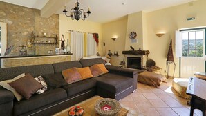 Una sala de estar con sofá, chimenea, pared de piedra y vistas por la ventana.