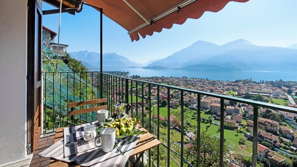 A balcony with a table set for breakfast, overlooking a mountainous landscape and a lake. - Vacation Apartment in Beautiful Vineyard 'Crotto Palma' with Lake View & Wi-Fi (Dongo)