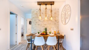 Un coin repas avec une table en bois, des chaises blanches, un centre de table composé de fruits et un luminaire fixé au mur.