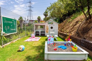 Un patio trasero cercado con área de juegos, una casita y un letrero de pizarra.