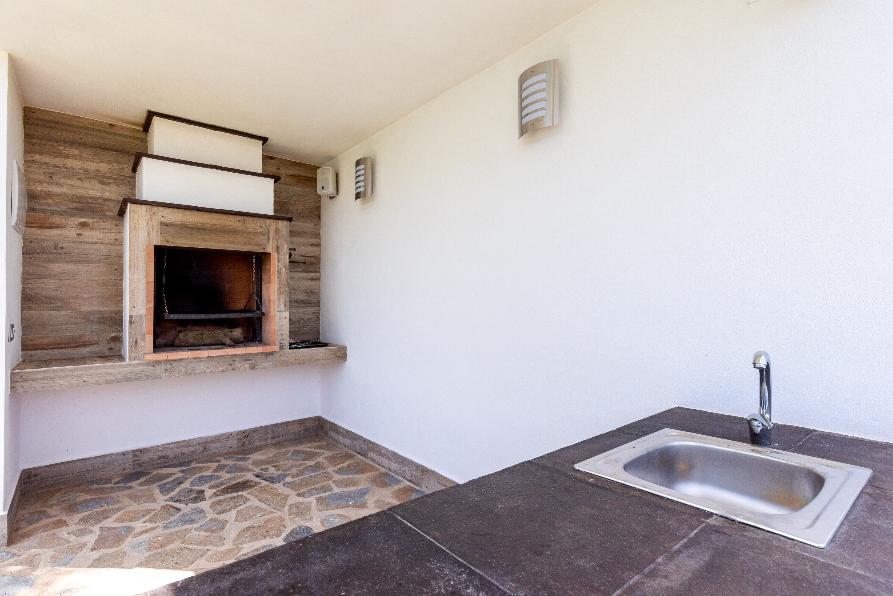 A kitchen with a stone floor, a built-in oven, a sink, and a wooden wall.