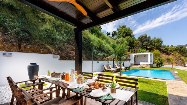 Un espace extérieur aménagé pour les repas, avec des meubles en bois, une piscine et une vue sur une colline.