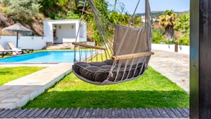 Une chaise suspendue près d’une piscine, avec un bâtiment blanc et de la verdure en arrière-plan.