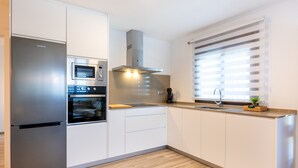 Une cuisine moderne équipée d’appareils électroménagers en acier inoxydable, d’un four encastré, d’un four à micro-ondes et d’une fenêtre avec des stores.