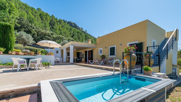 A swimming pool with a sun terrace, outdoor seating, and a mountain backdrop.