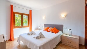 A neatly made bed with pillows, a bedside table with a lamp, and a window with curtains.