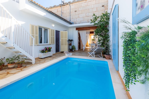 A swimming pool with a white staircase, potted plants, and a chair.
