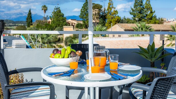 A round table with a white tablecloth, a bowl of fruit, and glasses of orange juice. - Vacation Home "Casa Cantino" with Pool, Wi-Fi & Terrace (Santa Margalida)