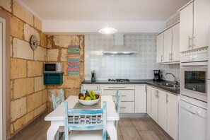 A kitchen with a stone wall, a clock, a microwave, a stove, and a sink.