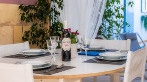 A dining table set with plates, glasses, and a bottle of wine, surrounded by chairs and plants. - Vacation Home "Casa Cantino" with Pool, Wi-Fi & Terrace (Santa Margalida)