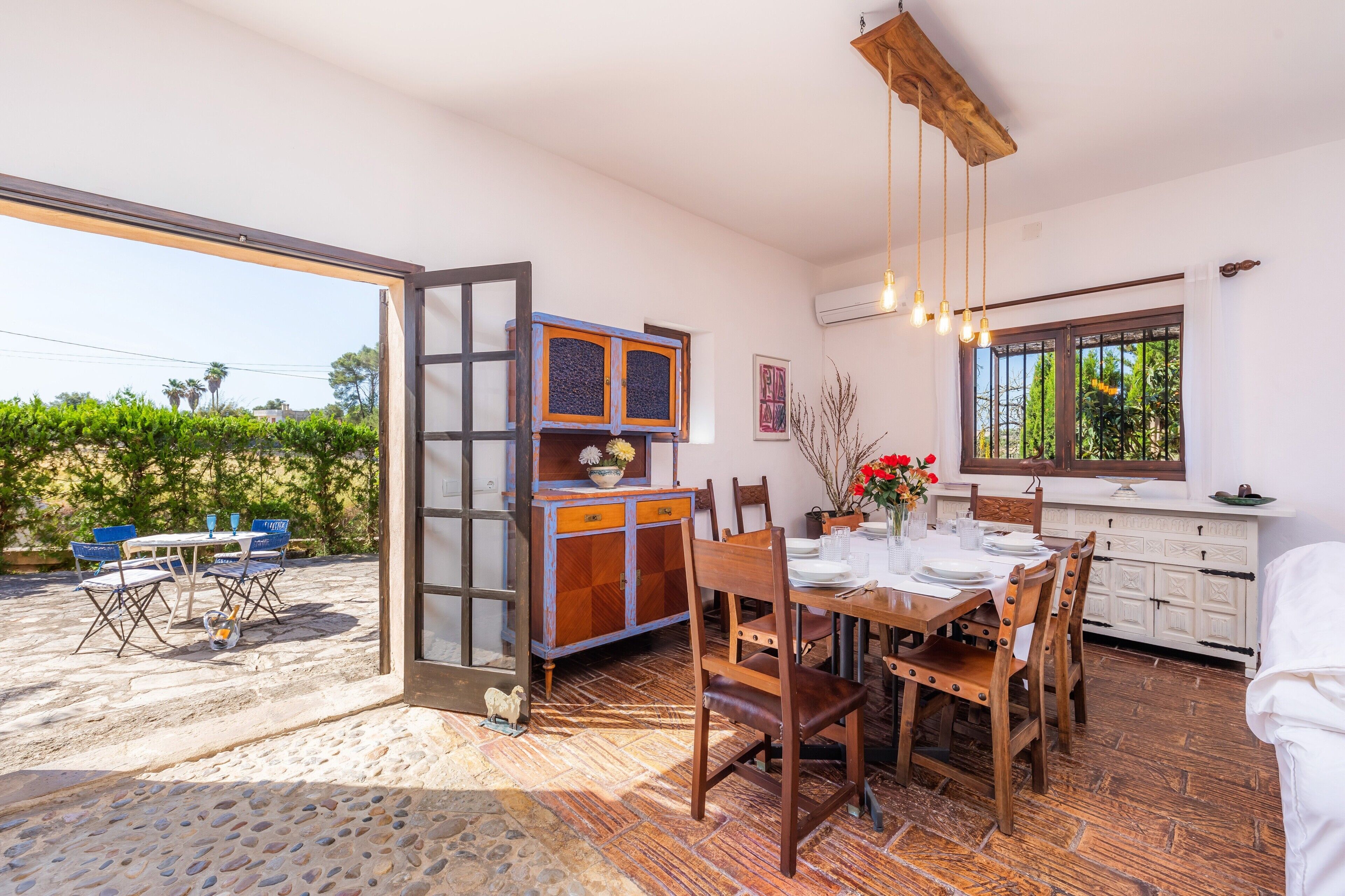 Un coin repas avec une table dressée pour quatre personnes, un buffet en bois et une fenêtre donnant sur un paysage verdoyant.