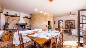 A dining area with a stone fireplace, wooden table, and chairs. - Pet-Friendly Vacation Home Moli Den Barret with Mountain View, Pool & Wi-Fi (Santa Margalida)