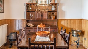 Una mesa de comedor de madera con sillas, una lámpara de cristal transparente en forma de cúpula y un armario de madera con diversos objetos.