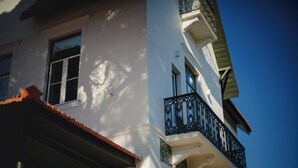 Un bâtiment blanc surmonté d’un toit recouvert de tuiles rouges, un balcon avec des balustrades noires, et un ciel bleu clair en arrière-plan.