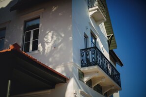 A white building with a red-tiled roof, a balcony with black railings, and a clear blue sky in the background. - A House In Estoril (Cascais)