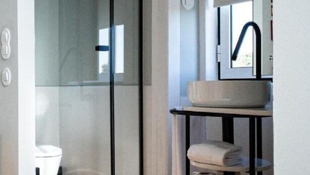 Une salle de bain moderne avec une paroi de séparation en verre, un lavabo blanc et un plancher en bois.