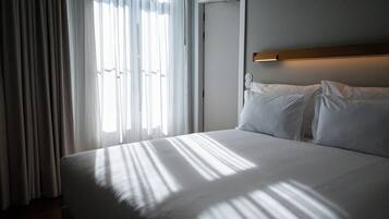 A neatly made bed with white linens, a wooden headboard, and a wall-mounted light fixture.