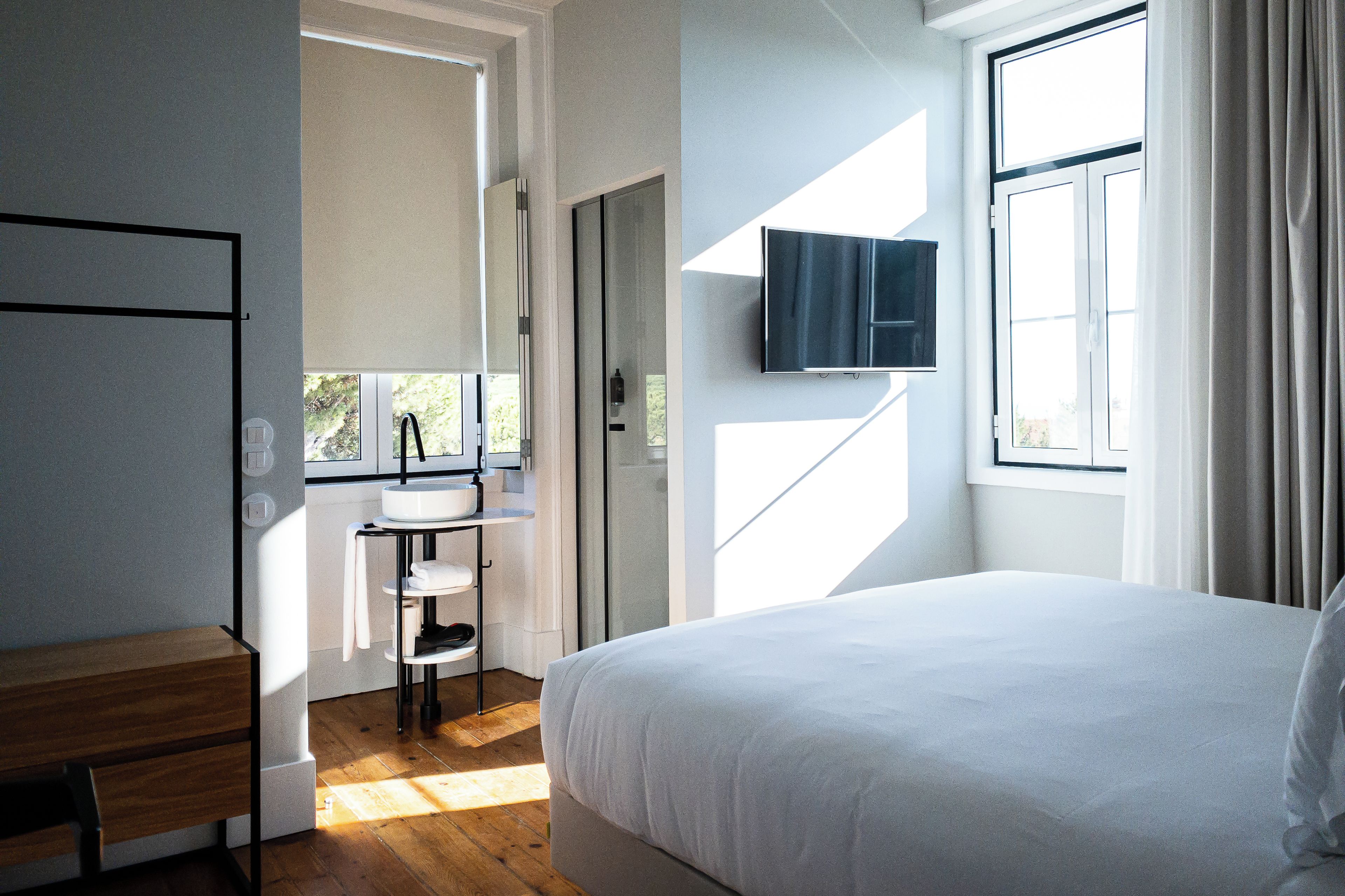 A modern bedroom with a large bed, a bedside table, a built-in TV, and a window with curtains.