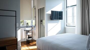 A modern bedroom with a large bed, a bedside table, a built-in TV, and a window with curtains.