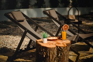 Two lounge chairs with a wooden table between them, a small potted plant, a bowl of fruit, and a glass of orange juice. - A House In Estoril (Cascais)