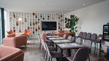A modern conference room with a long table, multiple chairs, a television, and a bookshelf.
