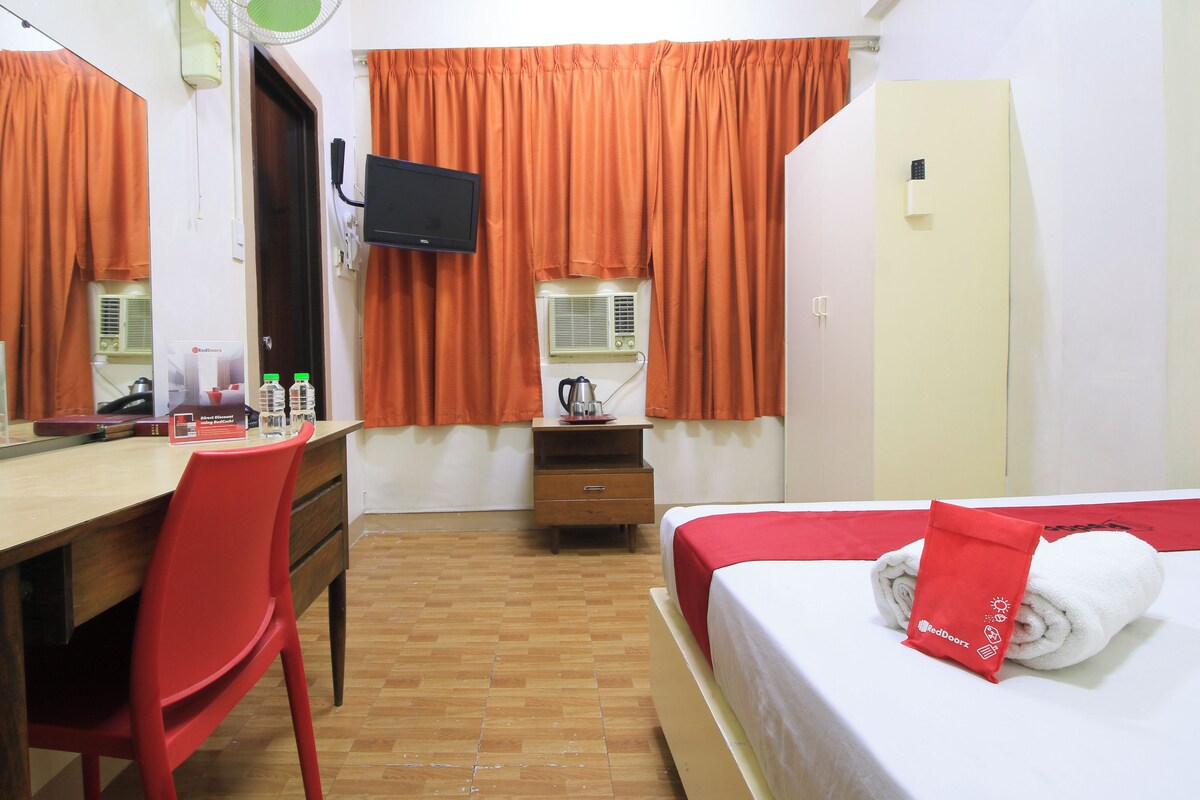 A hotel room with a bed, a desk, a chair, a television, and a wardrobe.