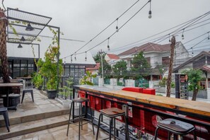 An outdoor seating area with a bar, potted plants, and a view of residential buildings. - Reddoorz @ Demangan Sari Residence (Depok)