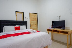 A bedroom with a bed, a television on a wooden stand, and two doors. - Reddoorz @ Demangan Sari Residence (Depok)