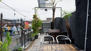 Un pequeño espacio al aire libre con una mesa y sillas, rodeado de plantas en macetas y una pared negra.