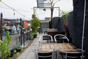 Un pequeño espacio al aire libre con una mesa y sillas, rodeado de plantas en macetas y una pared negra.