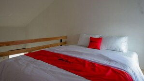 Una cama individual con cabecera de madera, ropa de cama blanca y un toque de color rojo.