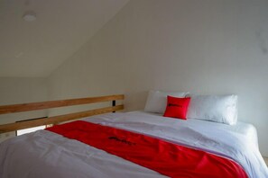 Una cama individual con cabecera de madera, ropa de cama blanca y un toque de color rojo.