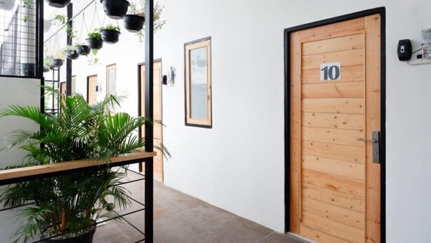A hallway with a wooden door marked '10', potted plants, and framed pictures on the walls. - Reddoorz @ Demangan Sari Residence (Depok)