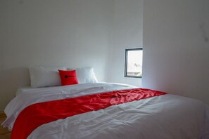 Un dormitorio con una cama, ropa de cama blanca y roja, y una ventana.