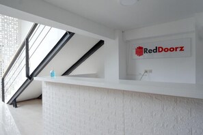 Una zona de recepció amb un taulell de recepció blanc, un logotip de RedDoorz i una escala amb baranes negres.