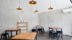A minimalist cafe interior with wooden tables and black chairs, featuring pendant lighting and a concrete wall backdrop. - Reddoorz @ Demangan Sari Residence (Depok)