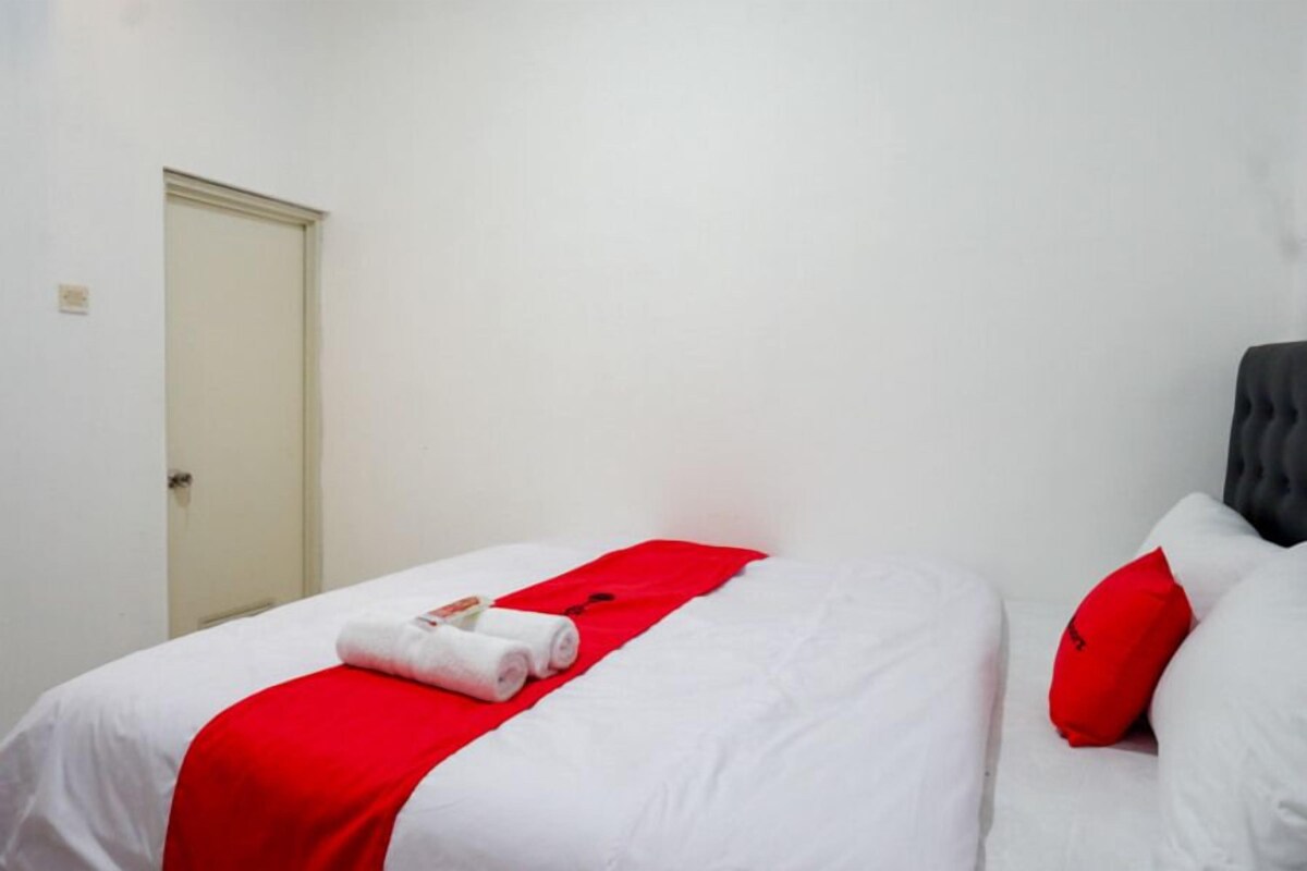 Una habitación de hotel con una cama, un edredón rojo y una almohada blanca.