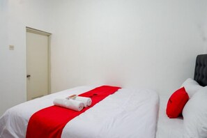 Una habitación de hotel con una cama, un edredón rojo y una almohada blanca.
