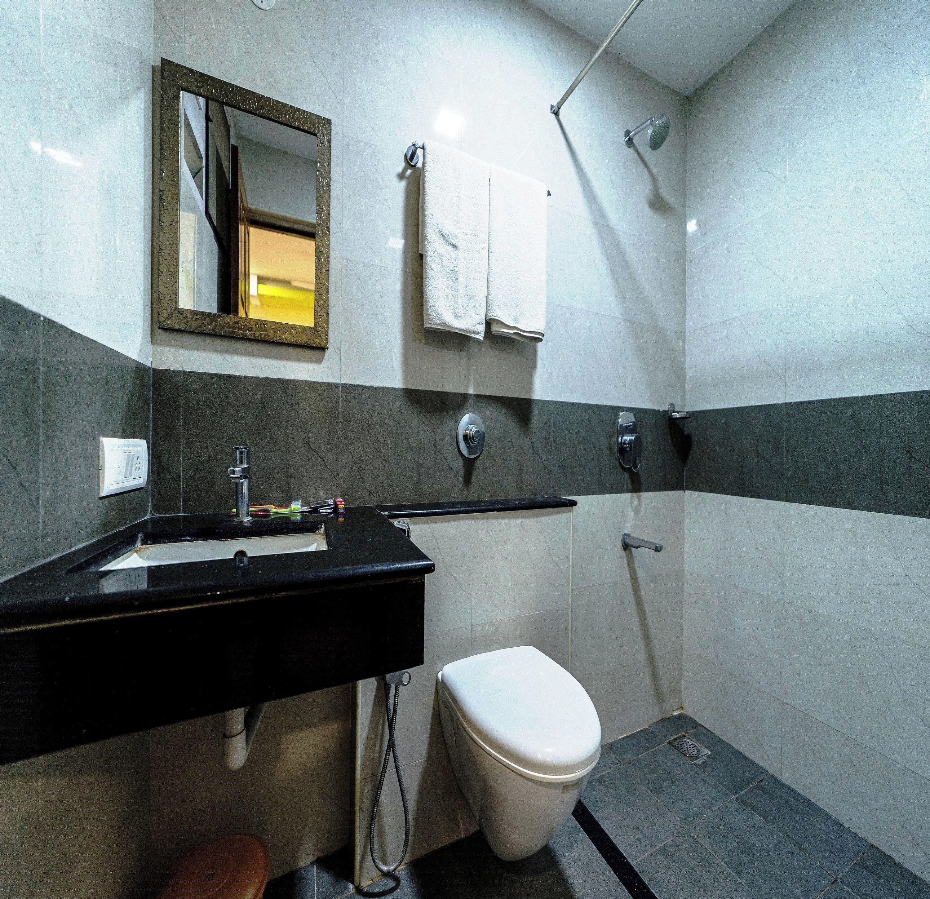 Een badkamer met een zwart wastafel, toilet, douche en spiegel.