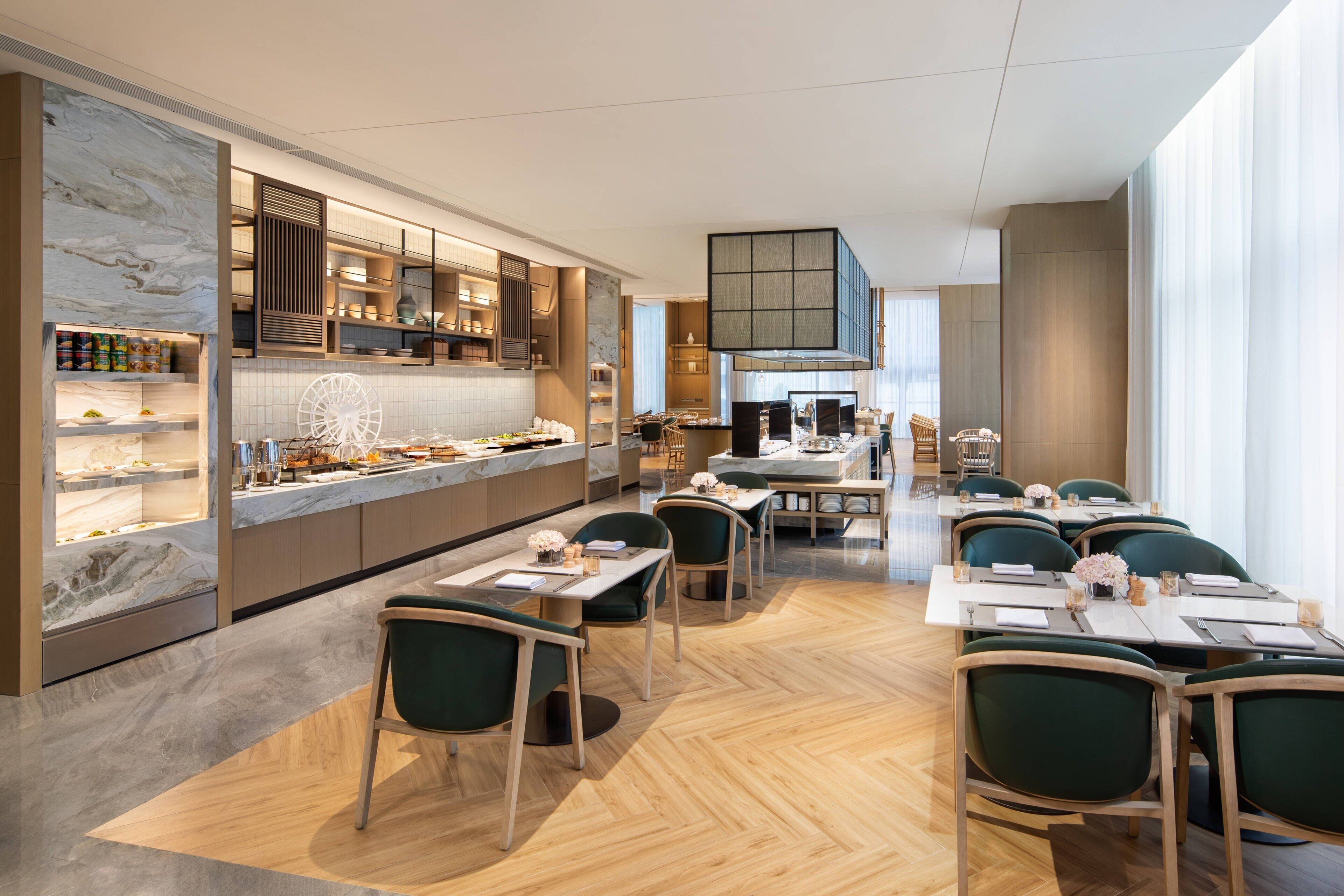 Un restaurante moderno con barra de mármol, armarios de madera y sillas tapizadas en verde.