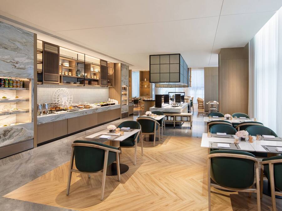 Un restaurante moderno con barra de mármol, armarios de madera y sillas tapizadas en verde.