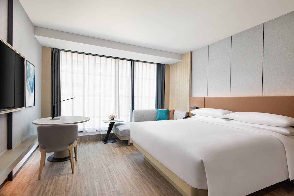 Ein modernes Hotelzimmer mit einem großen Bett, einem kleinen runden Tisch, einer Couch und einem Fernseher an der Wand.