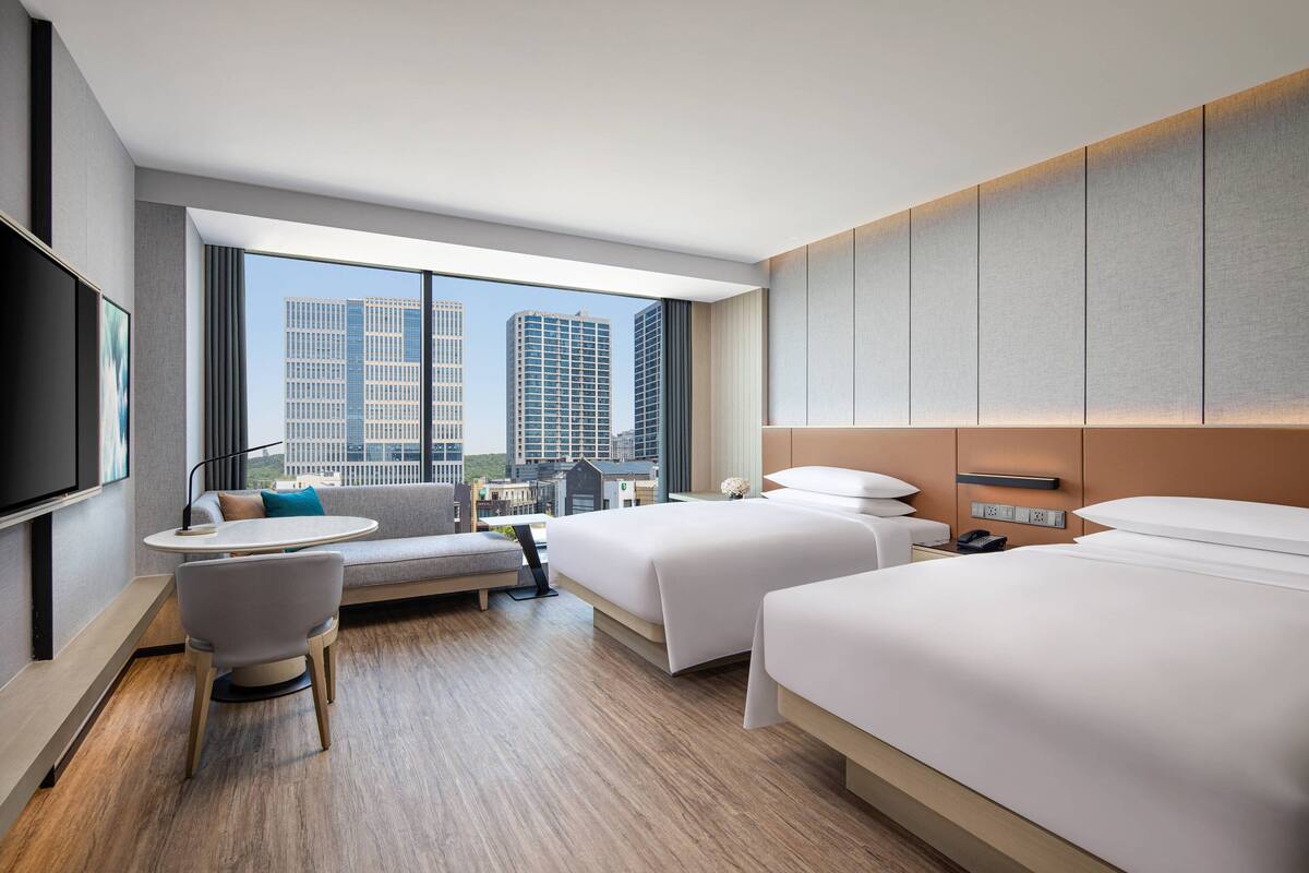 Ein modernes Hotelzimmer mit zwei Betten, einer Couch, einem Fernseher und Blick auf die Stadt.