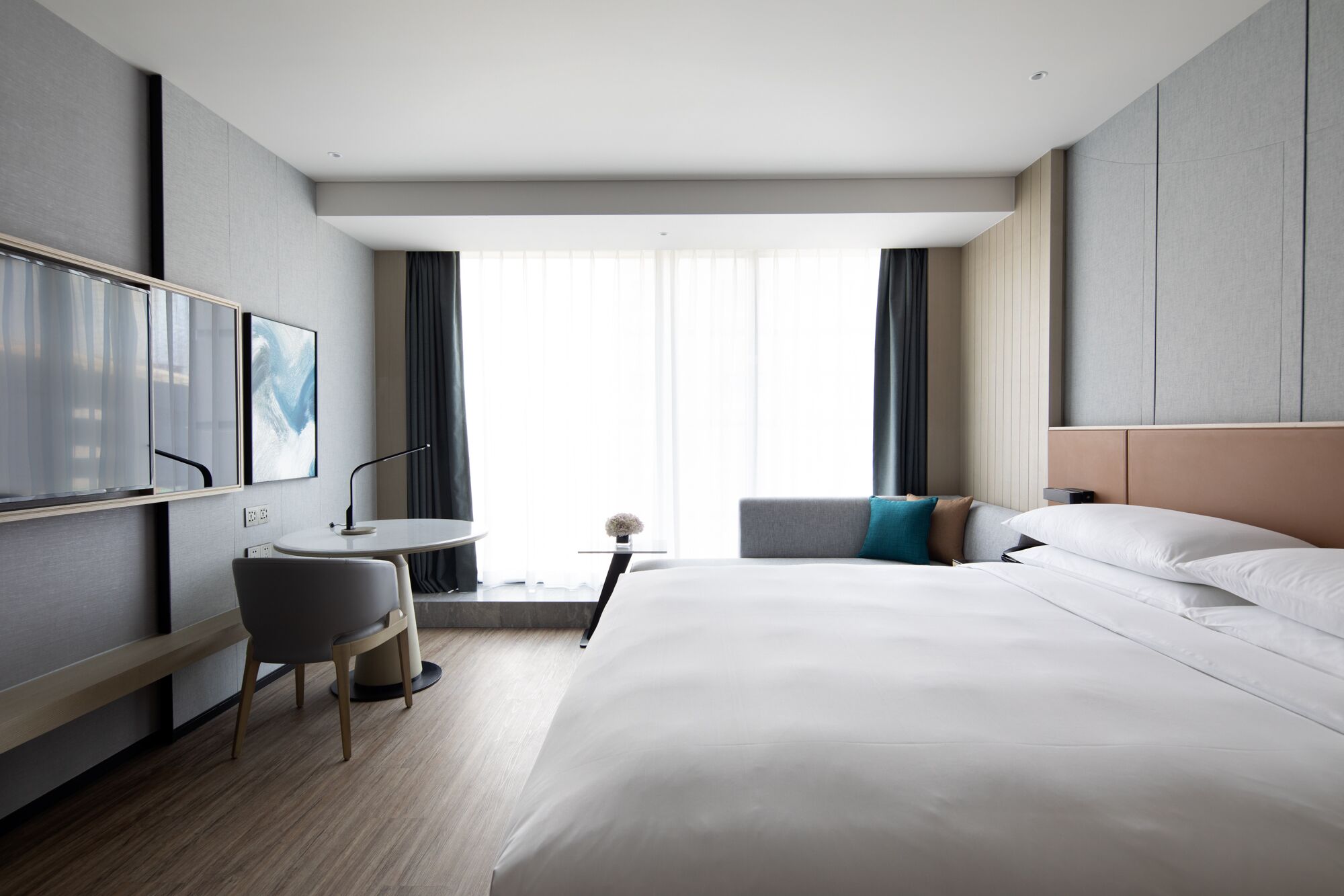 Una habitación de hotel moderna con una cama grande, un escritorio con silla, un televisor y una ventana con cortinas.