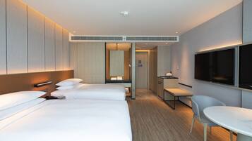 A hotel room with two beds, a desk, a chair, a TV, and a mirror.