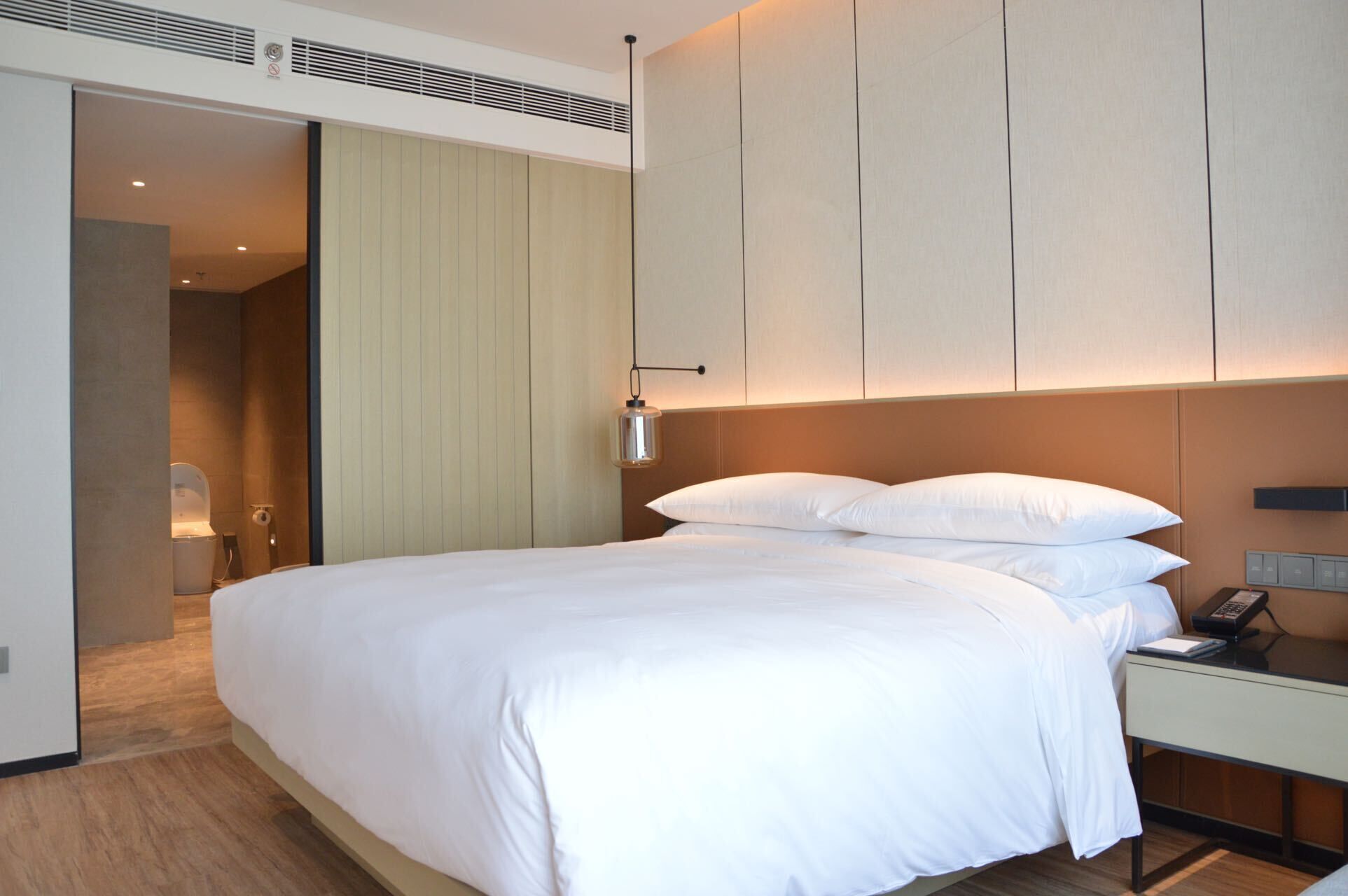 Habitació d'hotel moderna amb un llit gran, una tauleta de nit amb un telèfon i una làmpada de paret.
