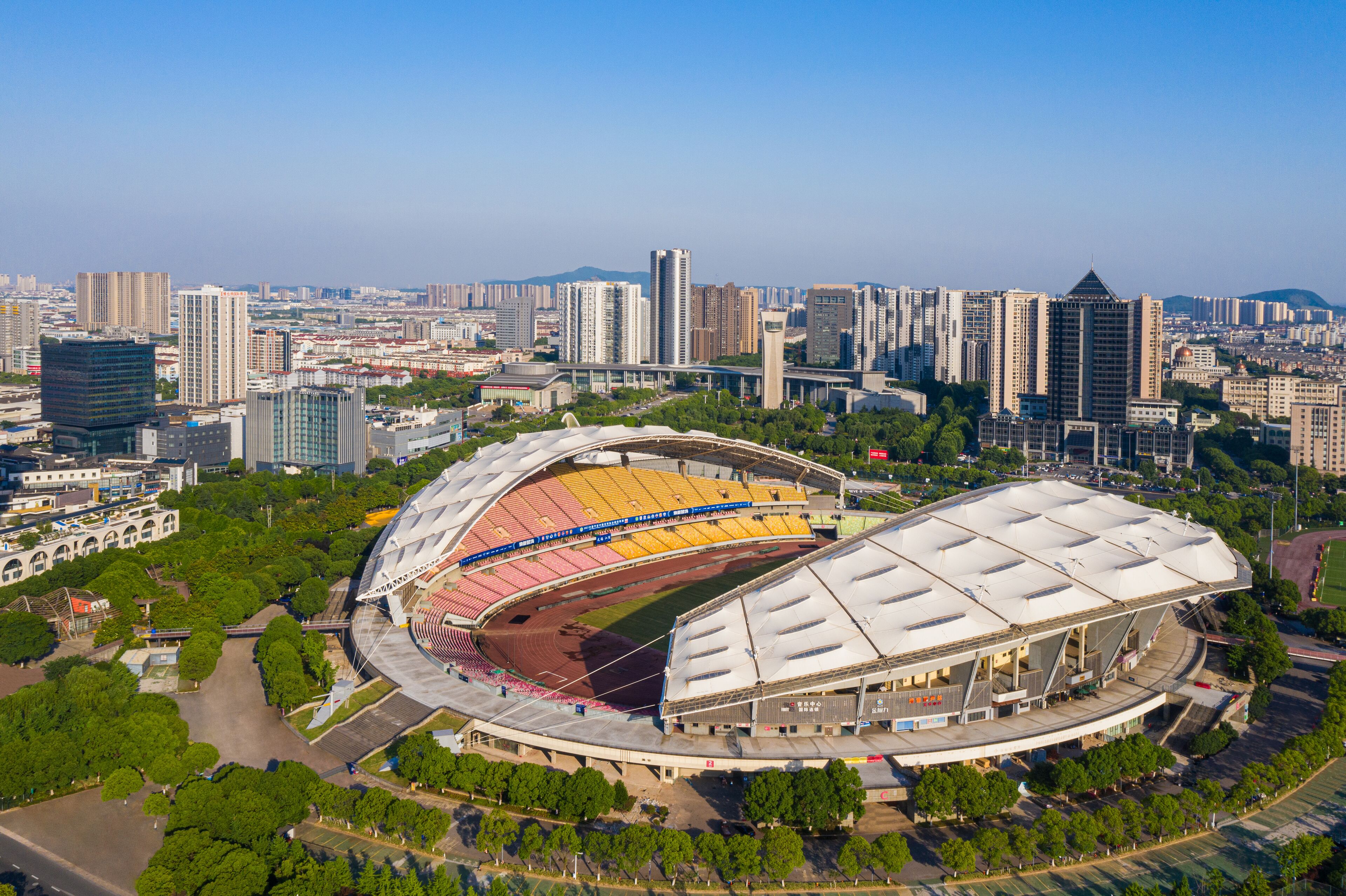 Un estadio grande con techo curvo, rodeado de edificios urbanos y vegetación.