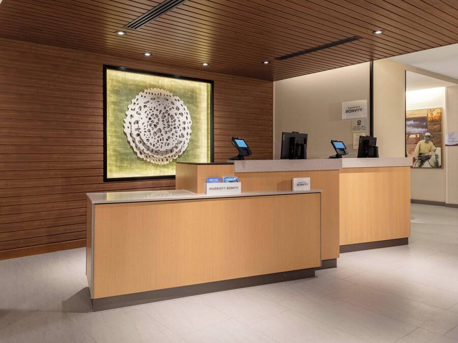 Una recepción de hotel con diseño moderno, que incluye un panel de pared de madera, una gran pieza decorativa en la pared y un quiosco digital.