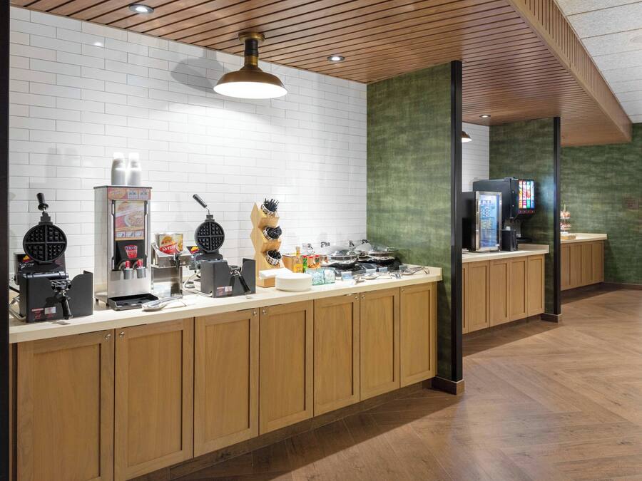 A modern kitchen area with a long counter, various appliances, and a wooden ceiling.
