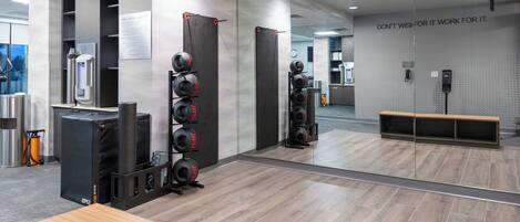 A modern gym with mirrored walls, weightlifting equipment, and a wooden reception desk.